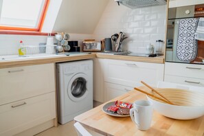 A modern kitchen with a washing machine, wooden countertop, and a bowl with chopsticks. - Apartment Sleeps 5 with Parking (Lairg)