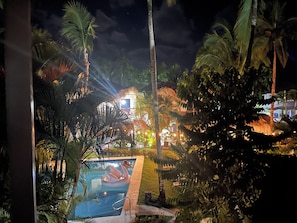 A nighttime view of a resort with a swimming pool, palm trees, and a building with illuminated windows.