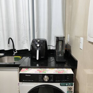Máquina de lavar roupa com painel de controle, cafeteira e pia em área de cozinha.