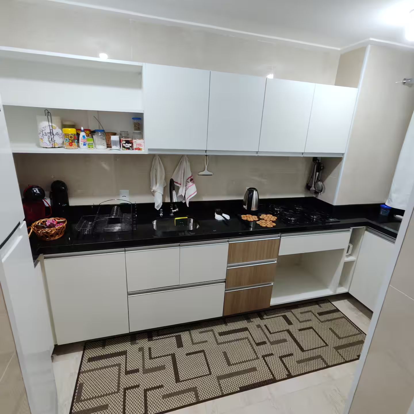 A modern kitchen with white cabinets, a black countertop, and a patterned rug.