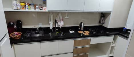 A modern kitchen with white cabinets, a black countertop, and a patterned rug.