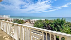 A balcony with a view of the ocean, a wooden deck, and tropical plants. - A-Frame in the Sand - Oceanfront + Pet-Friendly (New Smyrna Beach)