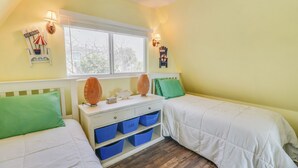 A bedroom with two beds, a nightstand, and a window with blinds. - A-Frame in the Sand - Oceanfront + Pet-Friendly (New Smyrna Beach)