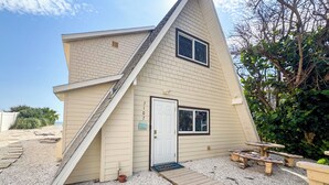 A house with a sloped roof, a front door, and a small porch area. - A-Frame in the Sand - Oceanfront + Pet-Friendly (New Smyrna Beach)
