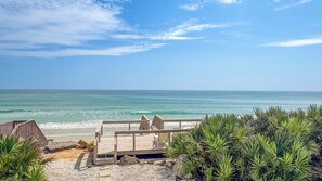 Una terraza de madera con vista a una playa, bajo cielos despejados.