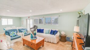 A living room with a sofa, chairs, a coffee table, and a TV. - A-Frame in the Sand - Oceanfront + Pet-Friendly (New Smyrna Beach)
