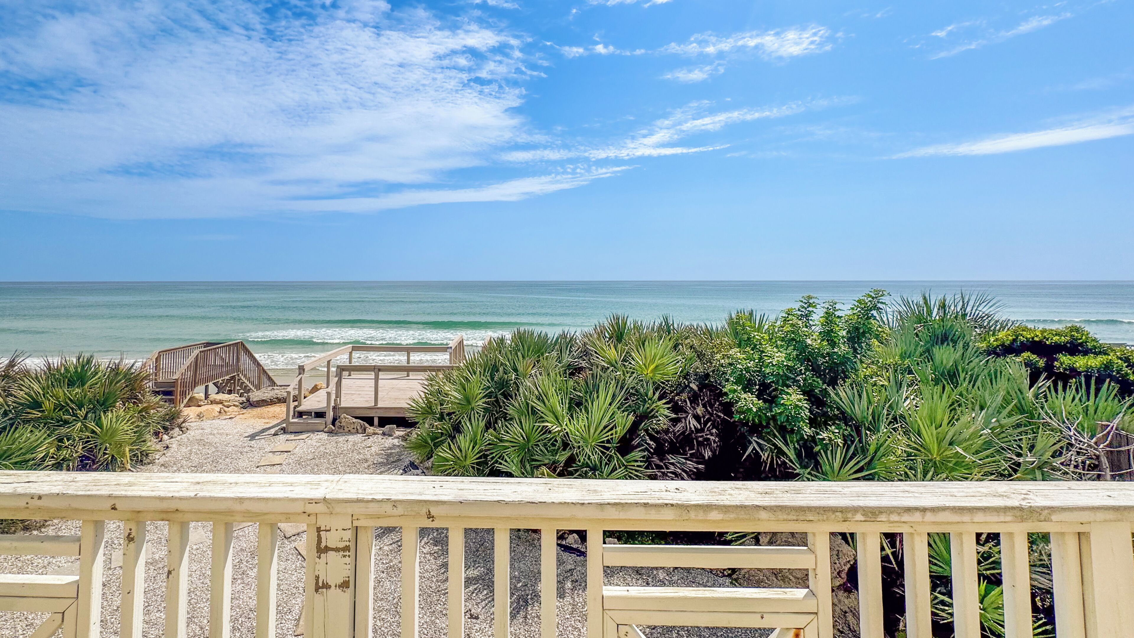 Vista a la playa con una terraza de madera y bancos frente al océano.