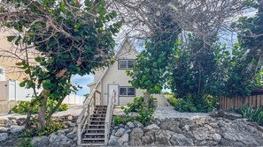 Una casa con una escalera de piedra que lleva a una puerta, rodeada de follaje y una cerca de madera.