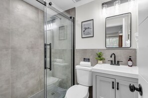 Ein modernes Badezimmer mit einer Duschkabine aus Glas, einer weißen Toilette, einem Waschbecken mit Spiegel und einem Schrank.