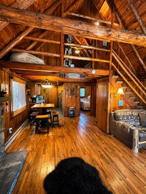A rustic cabin interior with a wooden dining area, a sofa, and a staircase. - Lake Harmony retreat with hot tub, sauna, game room, and ski access (Lake Harmony)