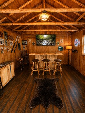 A rustic interior with wooden walls, a mounted television, a bar area with stools, and a fur rug on the floor. - Lake Harmony retreat with hot tub, sauna, game room, and ski access (Lake Harmony)