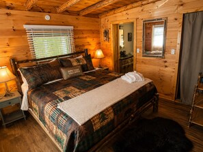 Une chambre confortable, aménagée dans un chalet en bois, avec un lit, des lampes de chevet, une petite table et un miroir.