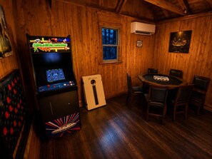 Une pièce avec un décor intérieur en bois, une table de billard, une borne d’arcade et un petit réfrigérateur.