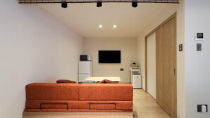 A compact room with a bed, a flat-screen TV, a microwave, and a small table with a basket. - Kaleido inn Hiroshima (Hiroshima)