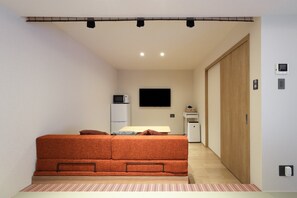 A compact room with a bed, a flat-screen TV, a microwave, and a small table with a basket. - Kaleido inn Hiroshima (Hiroshima)