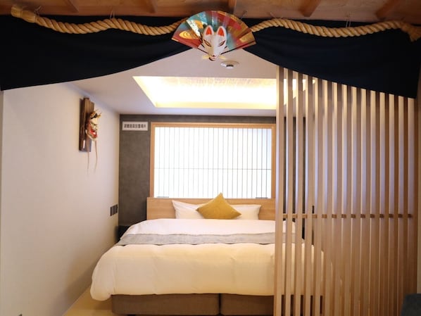 A bedroom with a bed, a window with blinds, a ceiling fan, and a decorative mask on the wall. - Kaleido inn Hiroshima (Hiroshima)