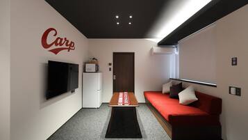 Una sala moderna con un sofá rojo, un televisor de pantalla plana montado en la pared, una mesa de centro y una puerta que da a otra habitación.