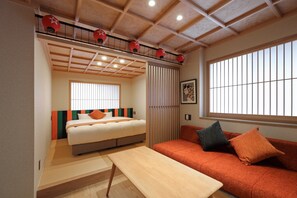 A compact room with a bed, a sofa, a small table, and a window with vertical blinds. - Kaleido inn Hiroshima (Hiroshima)