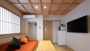 A room with a wooden ceiling, a sofa with cushions, a table, a television, a microwave, and a refrigerator. - Kaleido inn Hiroshima (Hiroshima)