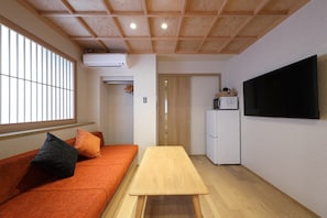 A room with a wooden ceiling, a sofa with cushions, a table, a television, a microwave, and a refrigerator. - Kaleido inn Hiroshima (Hiroshima)