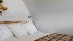 Ein Bett mit weißer Bettwäsche und einer karierten Decke, ein Holz-Kopfseitenverkleidung und eine wandmontierte Leuchte.