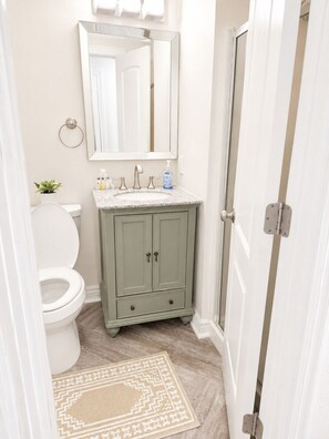 A bathroom with a toilet, sink, and cabinet, a mirror above the sink, and a door to the right. - Peaceful 2-bedroom condo with AC in Panama City Beach (Panama City Beach)