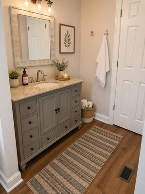 Un baño con lavamanos, espejo, toallero y una planta decorativa.