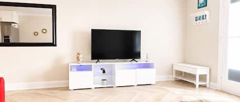 A modern living room with a flat-screen TV, white entertainment unit, and a large mirror.