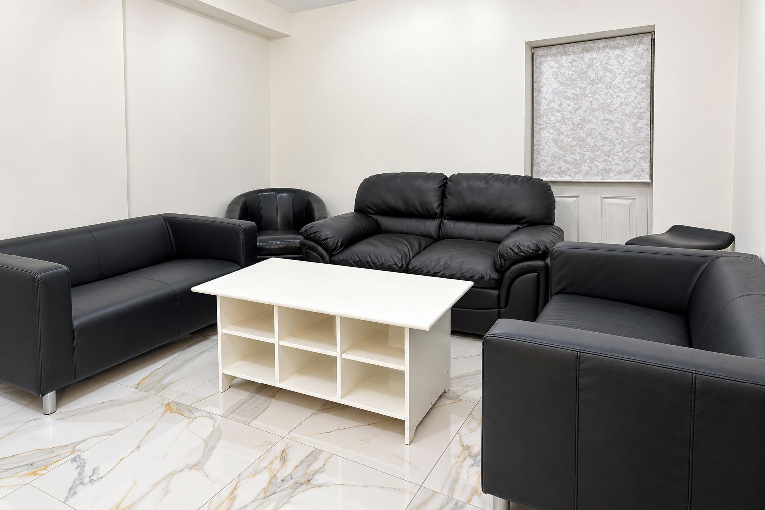 Una sala de estar moderna con sofás de cuero negro, una mesa de centro blanca y piso de baldosas de mármol.