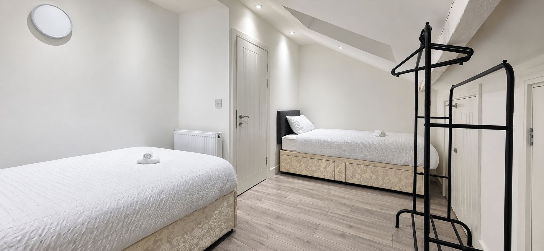 A bedroom with two beds, a radiator, a wardrobe, and a hanging rack.