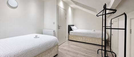 A bedroom with two beds, a radiator, a wardrobe, and a hanging rack.
