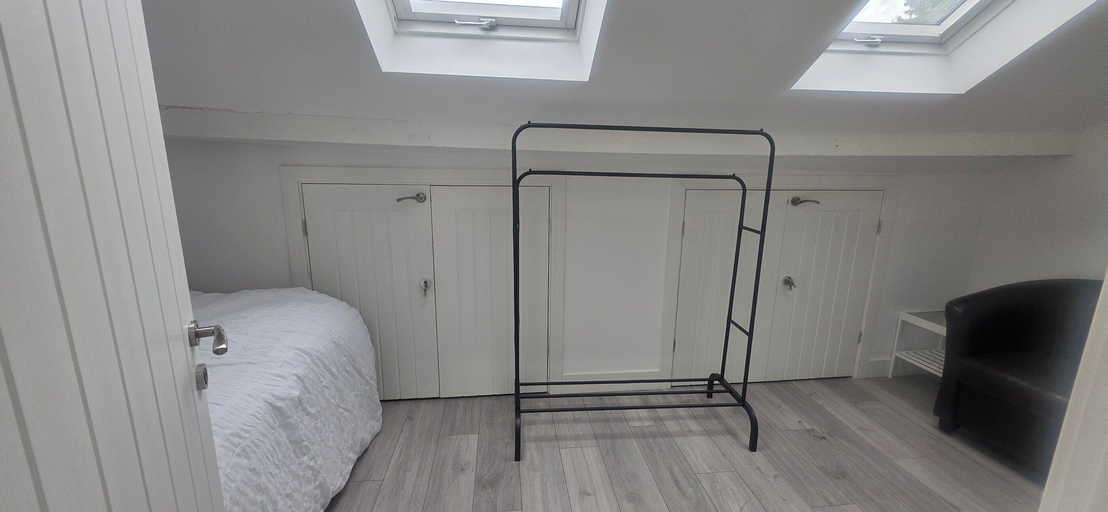 A bedroom with a skylight, a bed, a wardrobe, and a black chair.