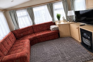 A cozy living room with a red sofa, a flat-screen TV, a lamp, and a small plant. - Spacious 6-Sleep Caravan | Includes own Driveway Space (Abergele)