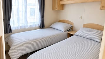 Habitació amb dos llits individuals, un panell de fusta al capçal, una petita taula de nit i una finestra amb cortines.
