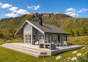 A modern house with a large deck, a chimney, and a mountainous backdrop.