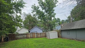A backyard with a wooden deck, a shed, and a house in the background. - 1910 Beautiful Craftsman Style Home (Topeka)