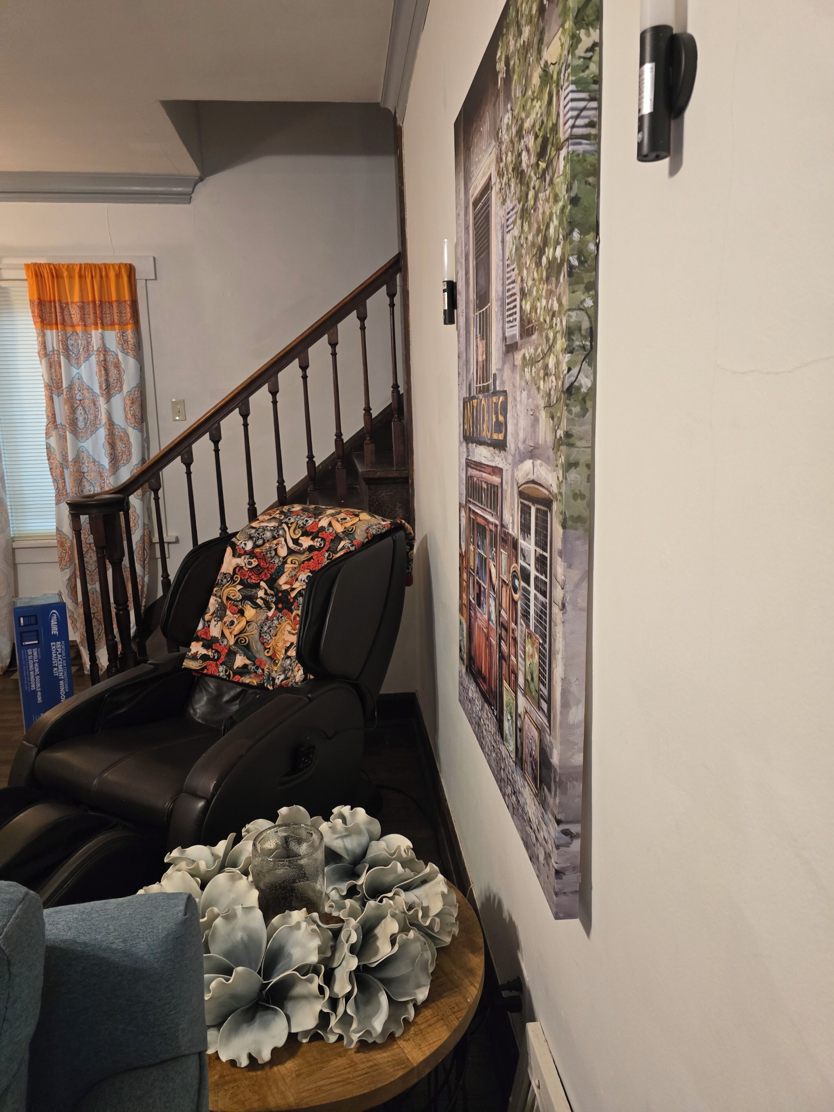 A staircase with a patterned throw blanket, a chair with a floral cushion, and a wall with an 'Antiques' sign.