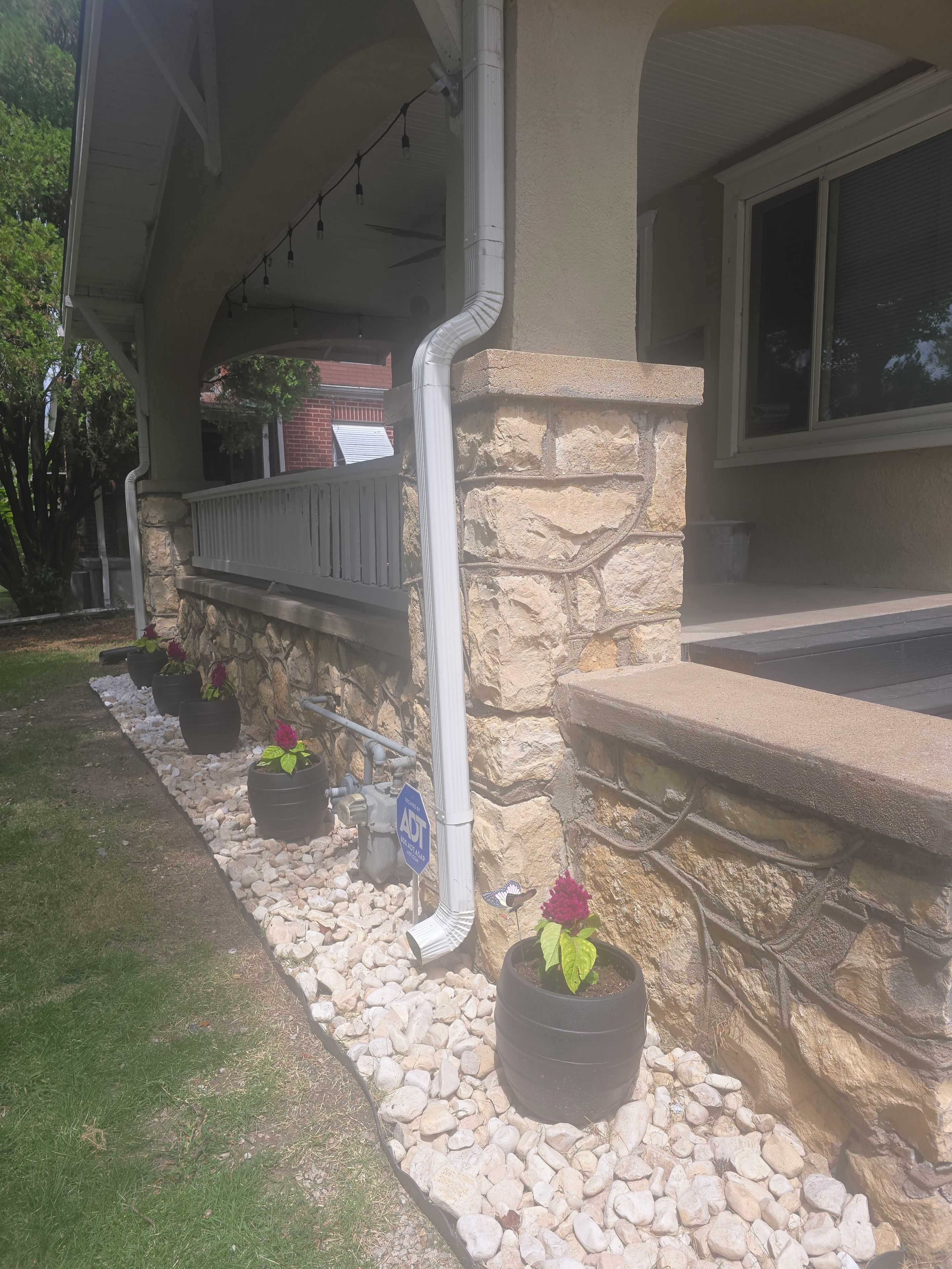 A house with a stone exterior, a porch with a railing, and potted plants along the walkway.