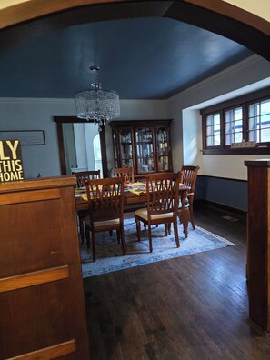 Une salle à manger avec un plafond sombre, une table à manger en bois, des chaises, un lustre et une fenêtre à carreaux.
