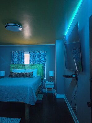 Ein Schlafzimmer mit einem Bett, Nachttischlampen, einem Beistelltisch, einem Fernseher und einem Fenster mit Vorhängen.