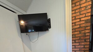 A room with a television mounted on a wall, a gray cushioned bench, and a patterned rug. - 1910 Beautiful Craftsman Style Home (Topeka)