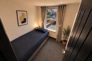 A small, single-bed room with a window, a framed picture on the wall, and a potted plant. - Tranquil Haven in Hornchurch - 3 bed house (Hornchurch)