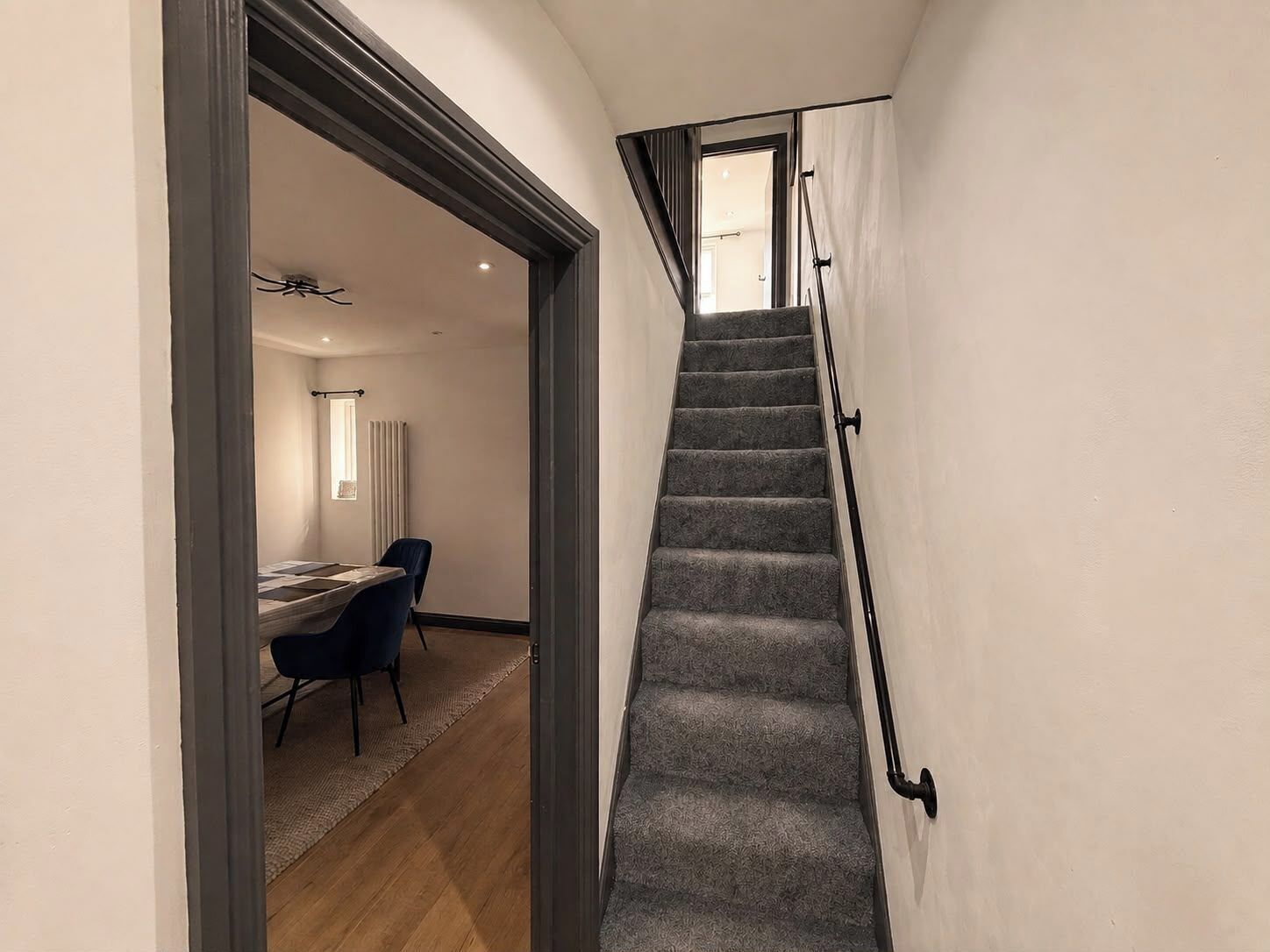 Un escalier dont les marches sont recouvertes de moquette et qui possède des rampes noires, menant à l’étage supérieur.