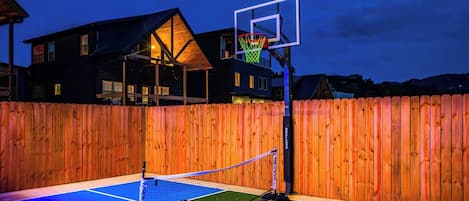Ein Basketballplatz im Freien mit Holzzaun, Basketballkorb und einem Tennisnetz.