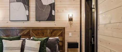 Une chambre à coucher avec une tête de lit en bois, un lit agrémenté de plusieurs oreillers et deux tableaux abstraits accrochés au mur.