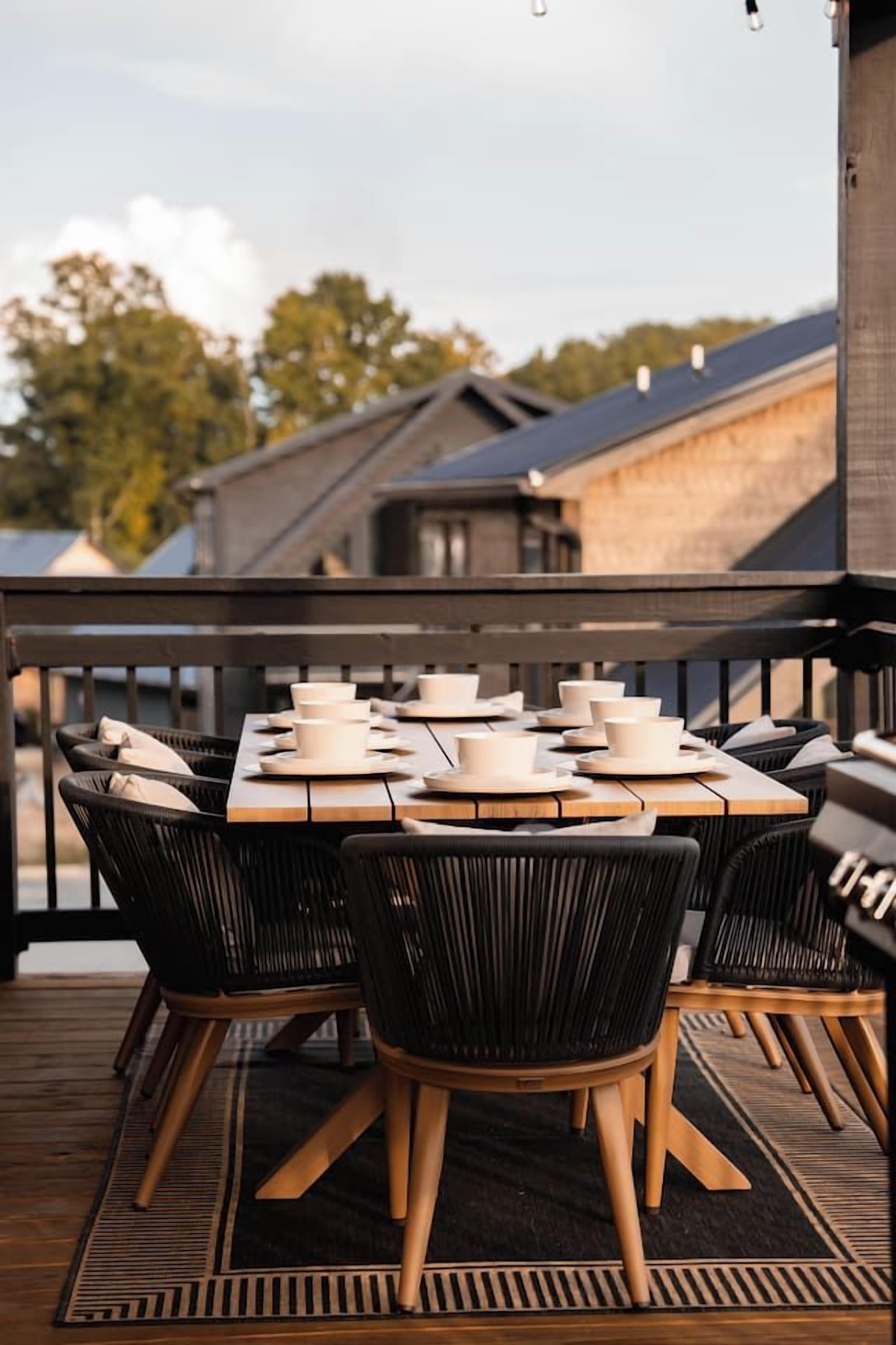 An outdoor dining area with a wooden table set for six, surrounded by black chairs with wooden legs.