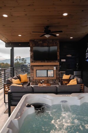 A modern interior with a stone fireplace, a large flat-screen TV, and a hot tub. - Luxury 6BR Cabin Sleeps 20 – Indoor Heated Pool, Golf Simulator, Sauna (Pigeon Forge)