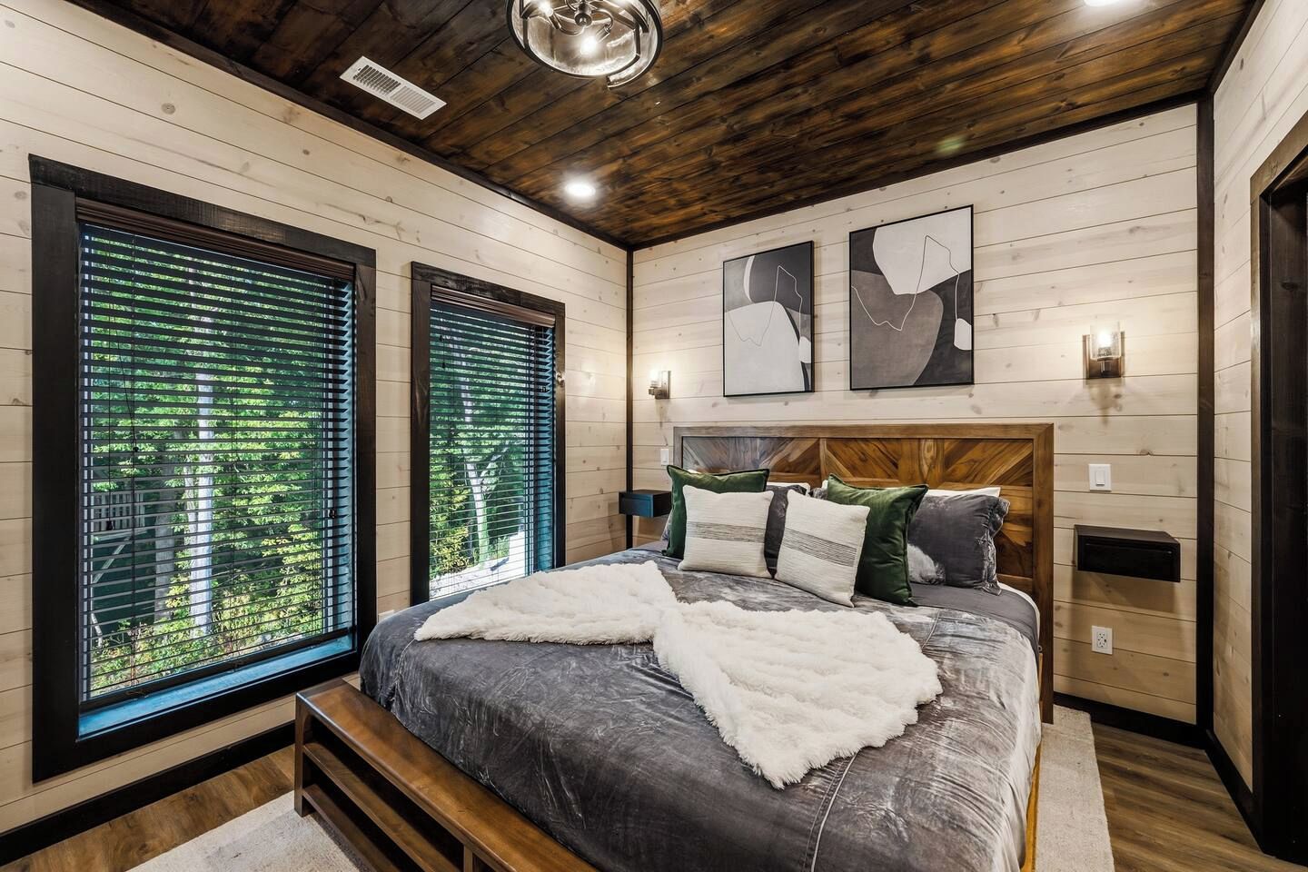 Une chambre avec un grand lit, des murs en bois et une vue sur la verdure par les fenêtres.