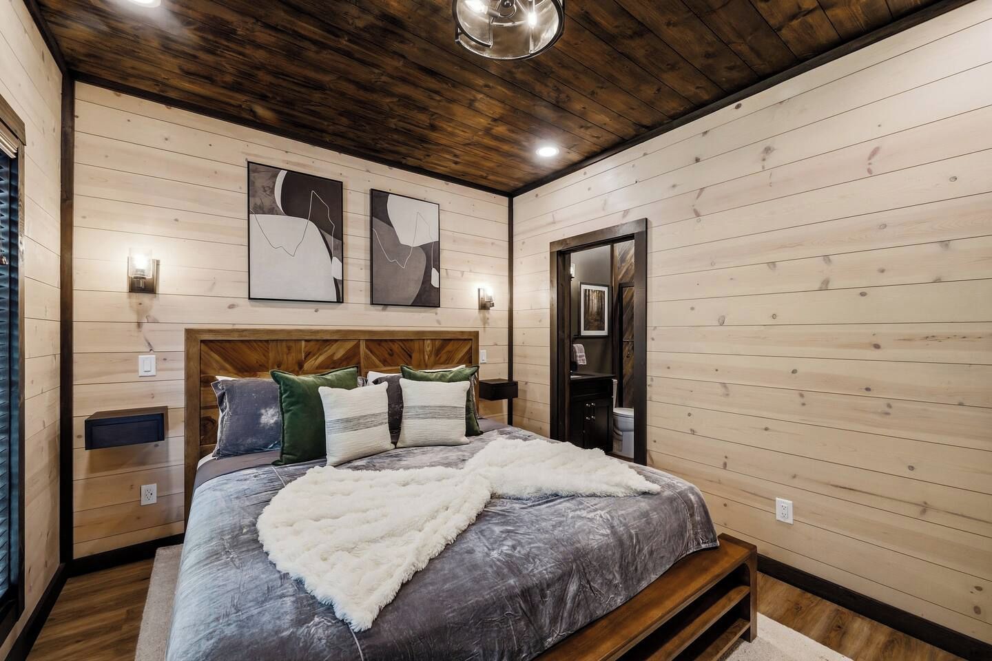 Une chambre à coucher avec une tête de lit en bois, un lit recouvert d’une couverture grise et deux œuvres d’art abstraites accrochées au mur.