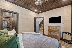 A bedroom with a bed, a television, a wardrobe, and a staircase. - New Host Special • Indoor Pool • Glow Court • Golf Sim • Rooftop Hot Tub • Sauna (Pigeon Forge)